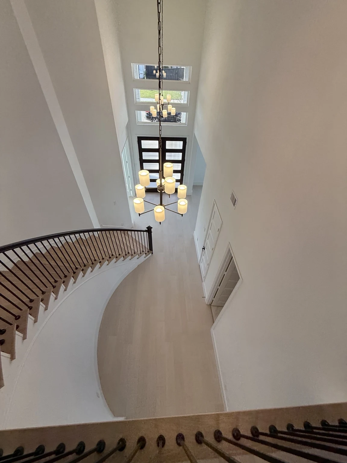 Curved staircase and chandelier above light engineered hardwood flooring