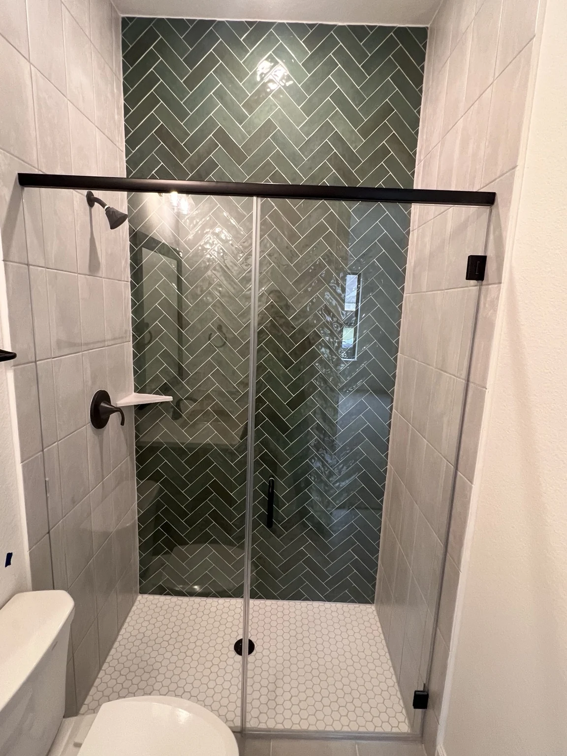 Glass shower enclosure with green herringbone accent tile